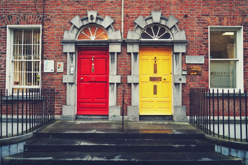 A bright red and a bright yellow Georgian front door side by side in a red-brick Dublin townhouse terrace