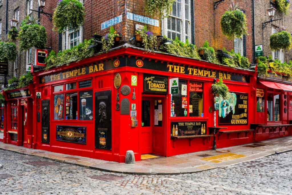 The bright red corner facade of The Temple Bar pub in Dublin, hung with flowers and signs