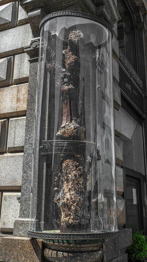 Medieval tree trunk studded with nails, displayed under glass on a Vienna street corner